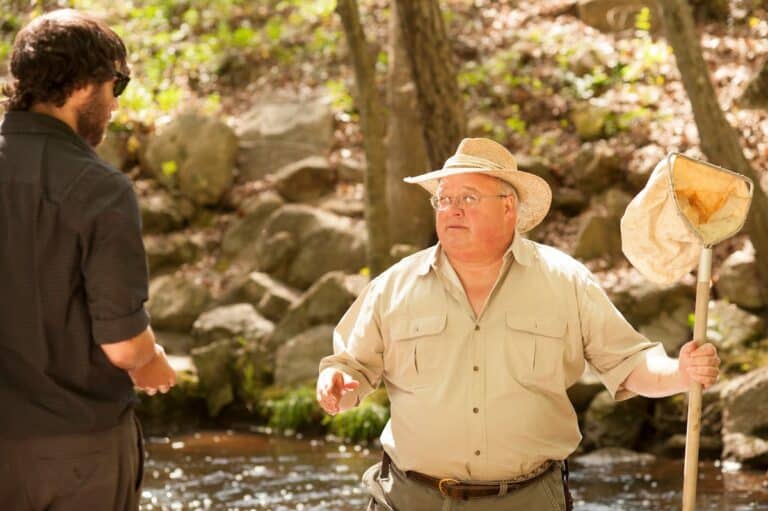 Dr. Richard Groover stands next to river holding a net while speaking to young man