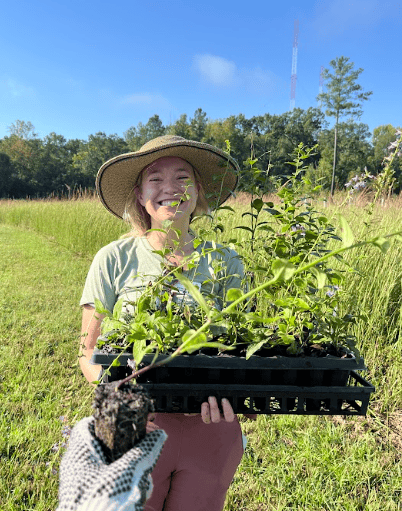 CRLC Land Stewardship Manager holds a tray of plants in an outdoor setting